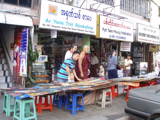 A sinewy monk in saffron leans over a table with booksellers at Yangon's bustling Bogyoke market.